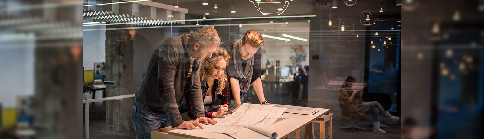 Three designers lean over a set of plans on a table