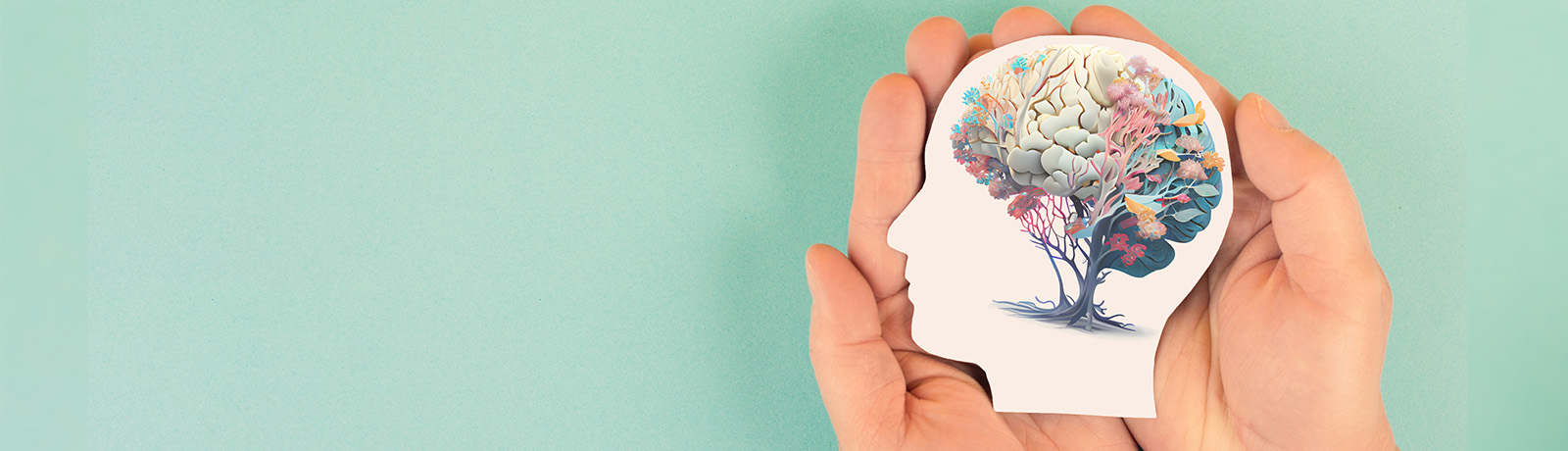 Stock image of a person's hands holding a paper cut-out of a head with an illustrated brain