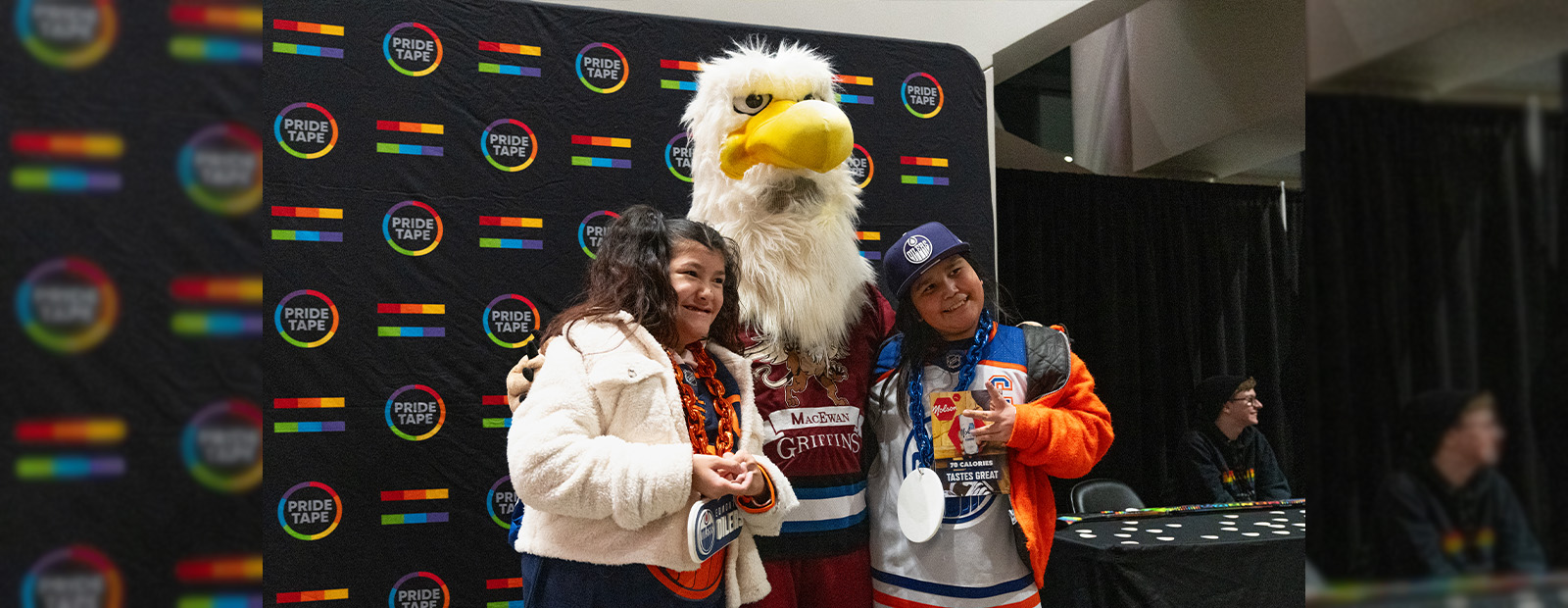 Two people stand with the Griff mascot at the Oilers Pride game