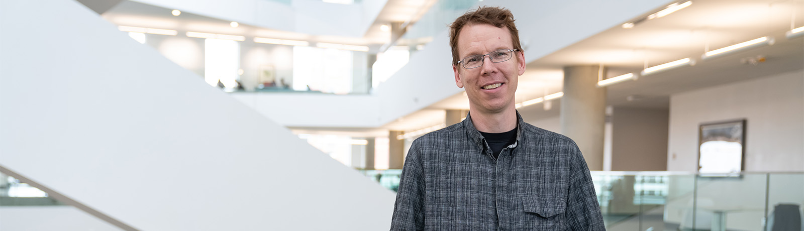 Dr. Kevin Judge leans against a glass railing in Allard Hall, smiling.