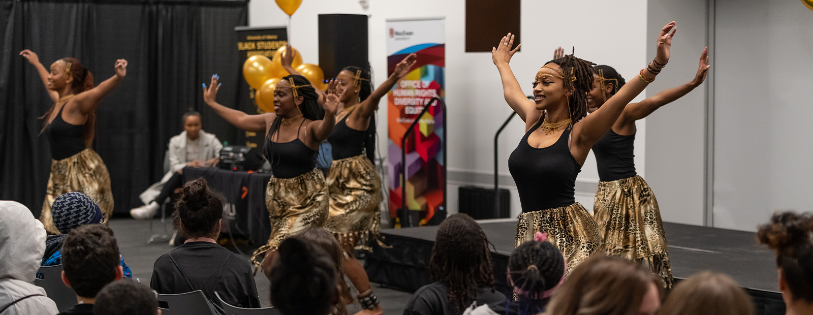 Performers dancing in front of a crowd of seated people at a Black History Month event.