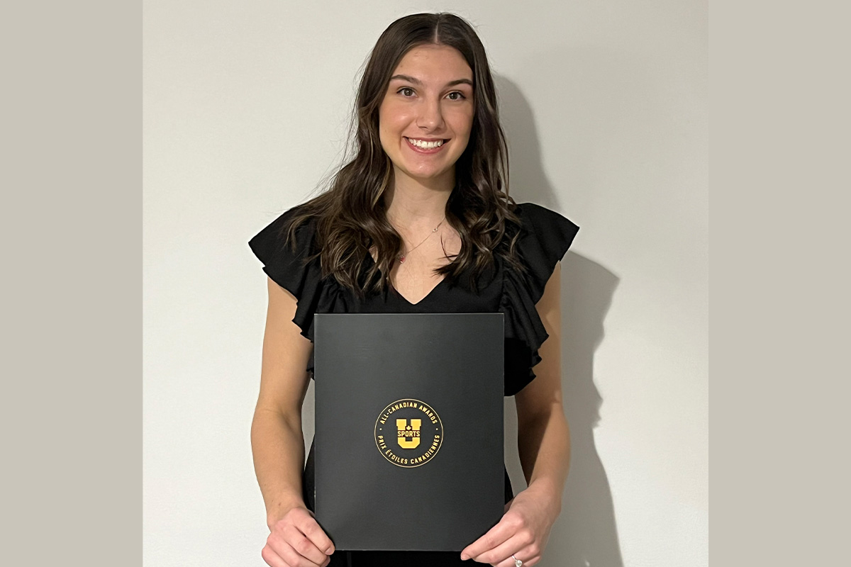 Mariah Bereziuk holds a U SPORTS certificate, smiling, standing in front of a grey wall