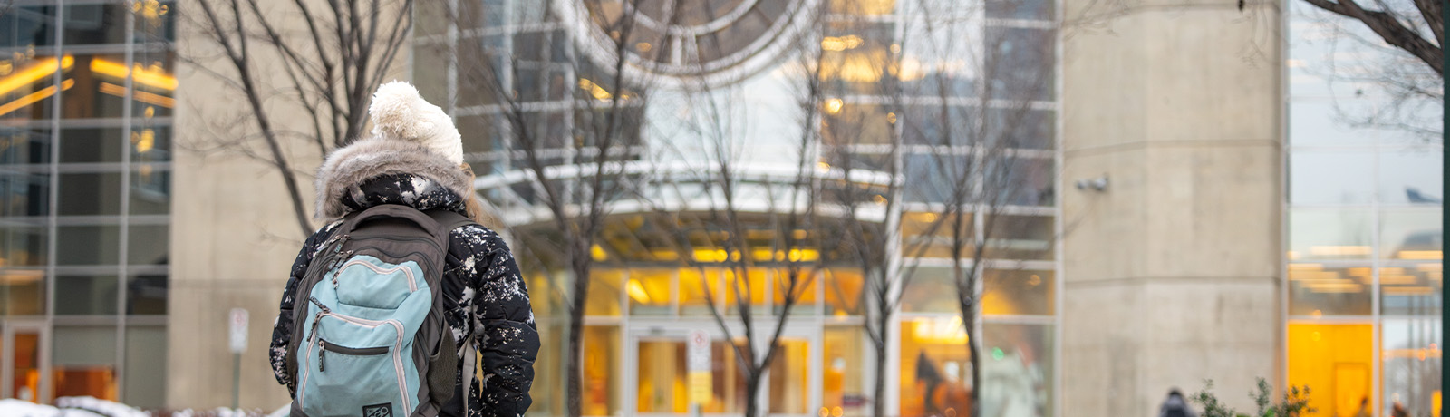 A female student walks toward the clock tower entrance to campus wearing a backpack.