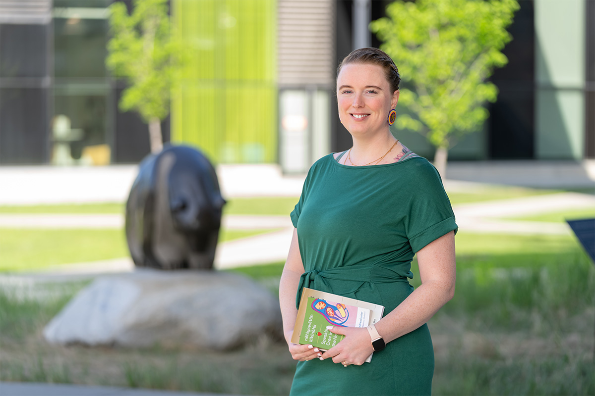 Allyson Brinston holds a Cree book and stands in front of the Treaty 6 marker on campus.