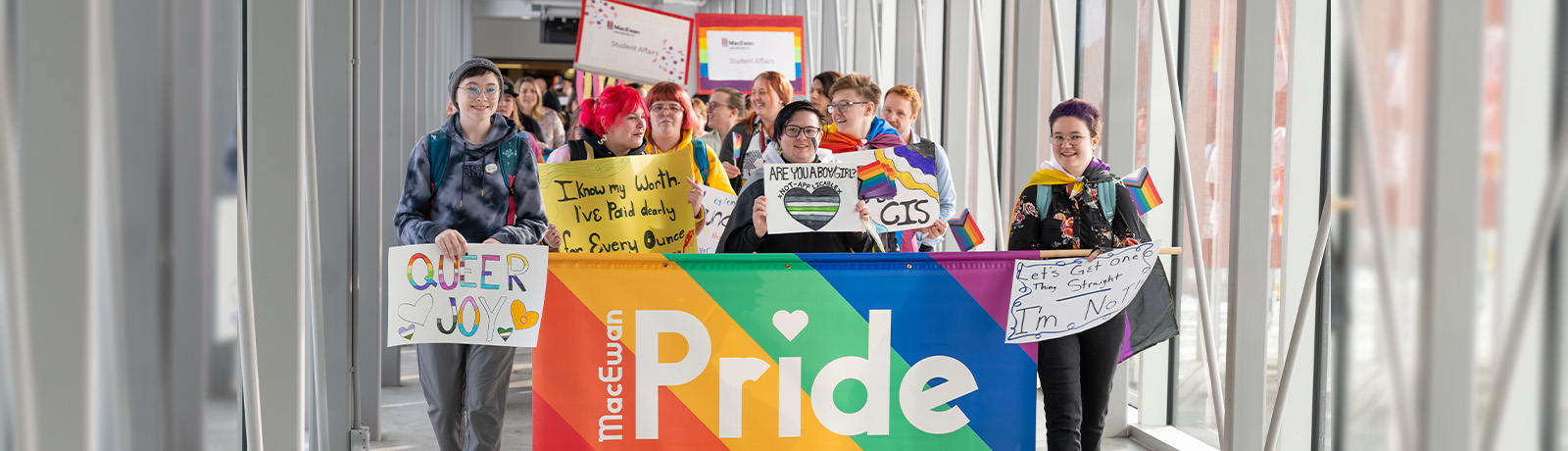 A group of students walking along a pedway holding a large banner that reads MacEwan Pride, along with other smaller signs