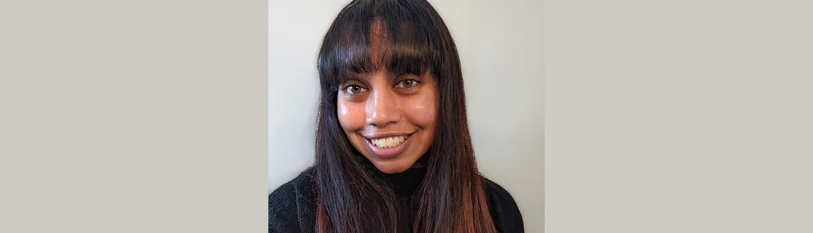 Tisha Raj stands in front of a grey wall and smiles.