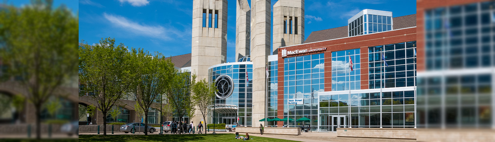 Students sit on the lawn in front of Building 7 as the sun shines on the MacEwan building.