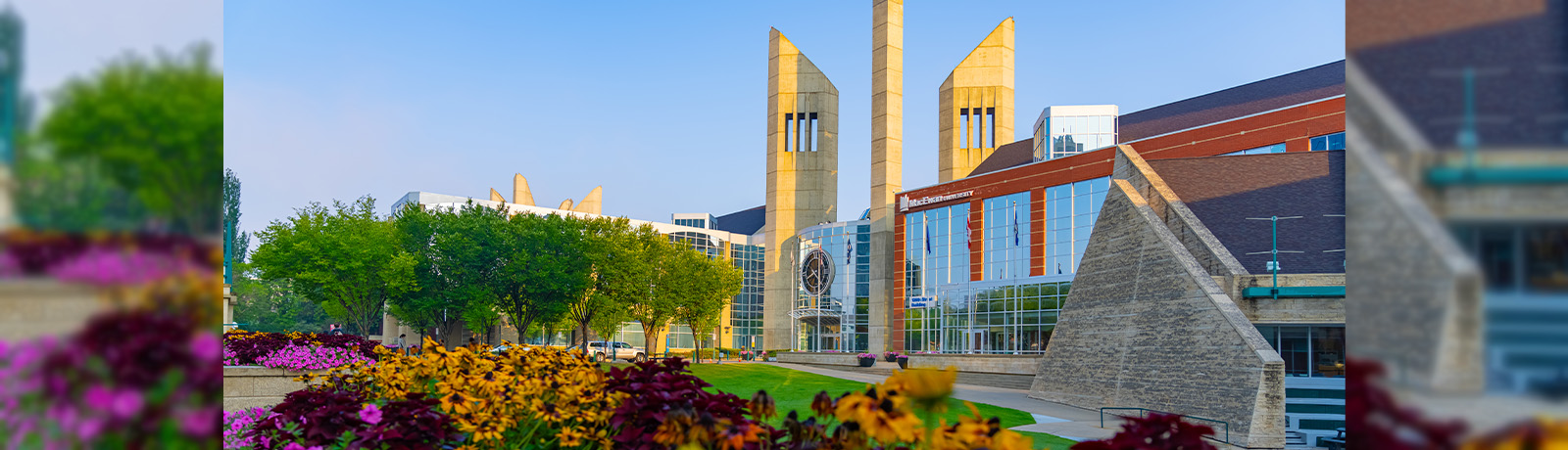 MacEwan's clocktower entrance seen at sunrise, with colourful flowers in the foreground.