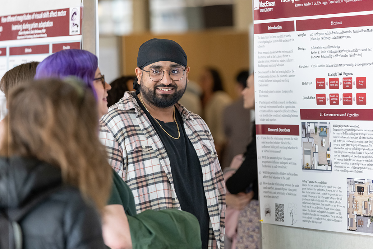 A student stands in front of a poster display, discussing his work.