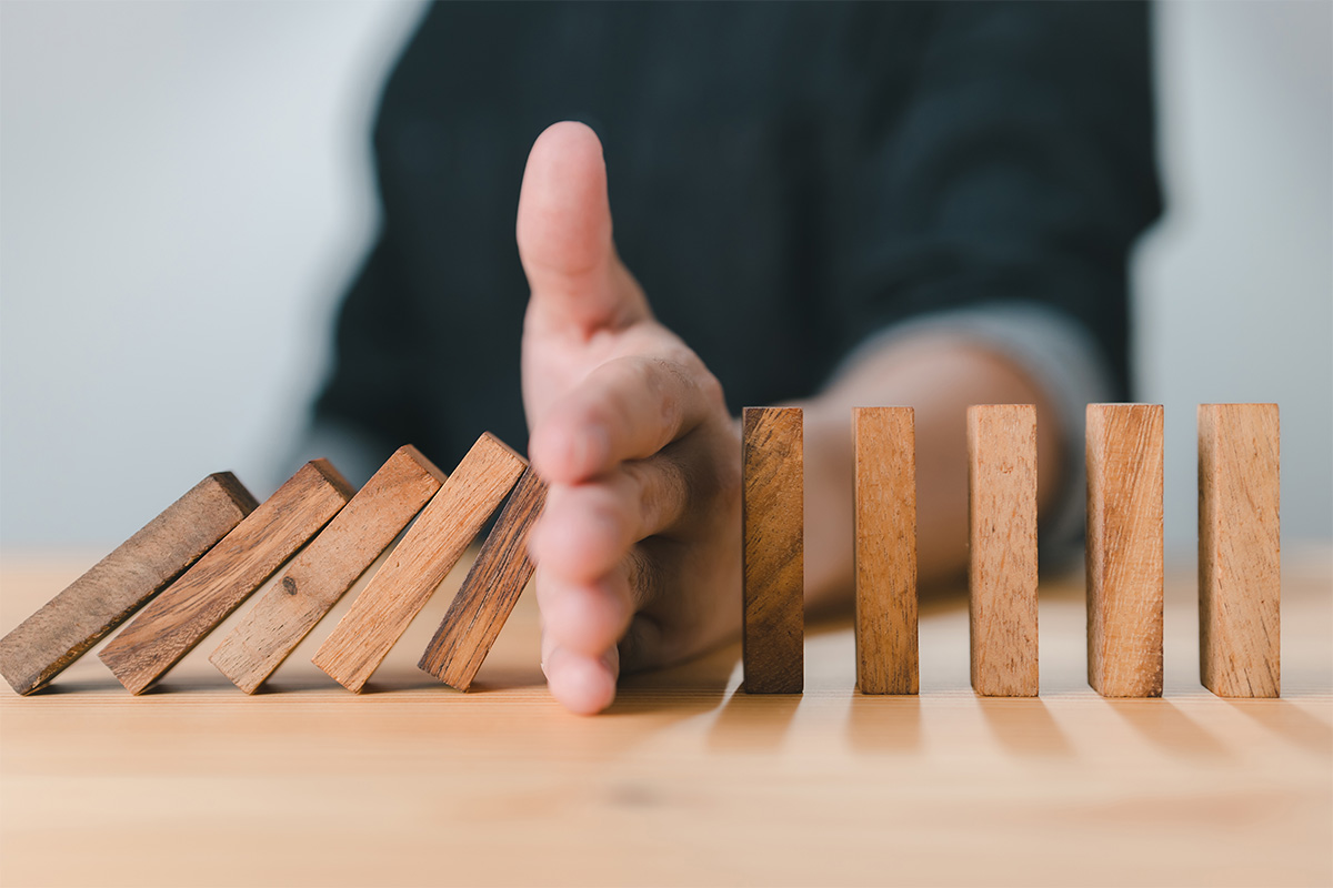 A hand stops a row of falling dominoes, leaving others standing upright