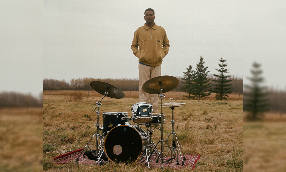 Biboye Onanuga stands behind a drum kit in the middle of a field.