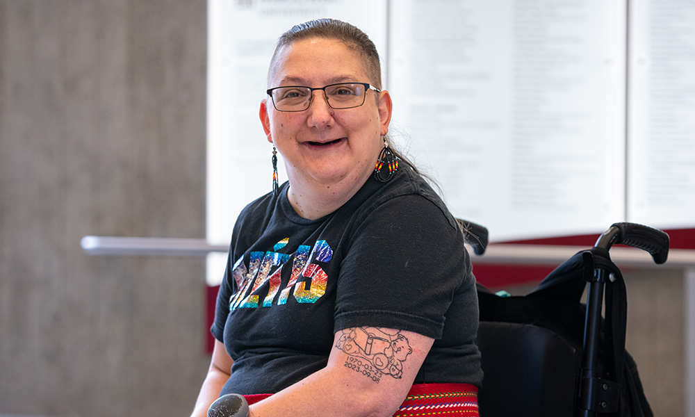 Al Olsen sits in their wheelchair in Building 6 and smiles.