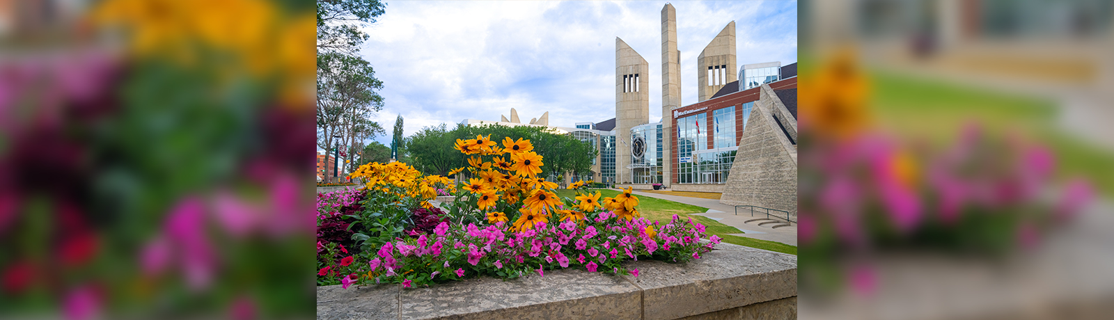 MacEwan's main entrance, with the clock tower in the background and a garden bed of pink and orange flowers in the foreground