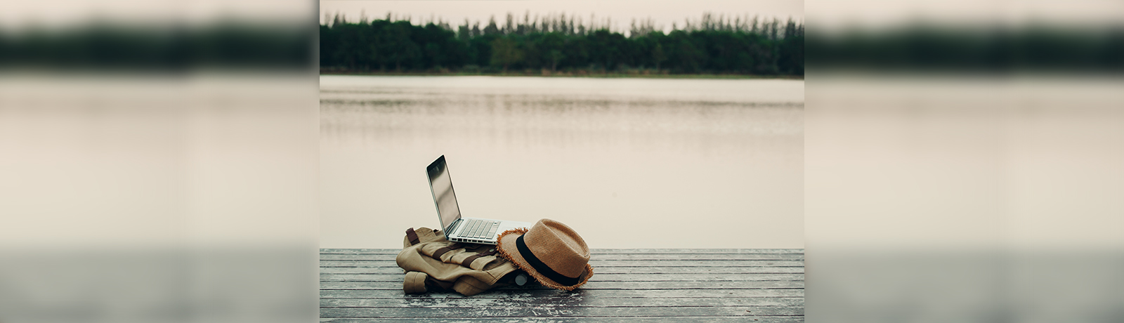 Laptop open on top of a tan-coloured backpack on top of a dock with a lake in the background.