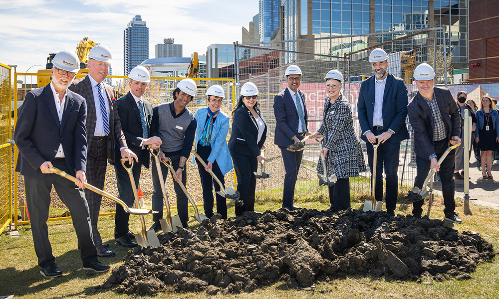 Several people wear hard hats and hold shovels at the site of the new School of Business building