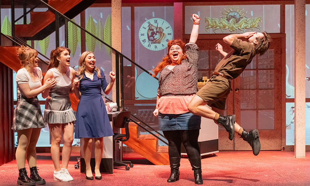 On stage, a woman raises a fist excitedly and a man falls back, having been hit.
