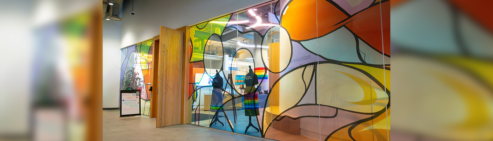 The front entrance of kihew waciston Indigenous Centre, its doors and glass windows, which are covered with images of colourful, faceless people