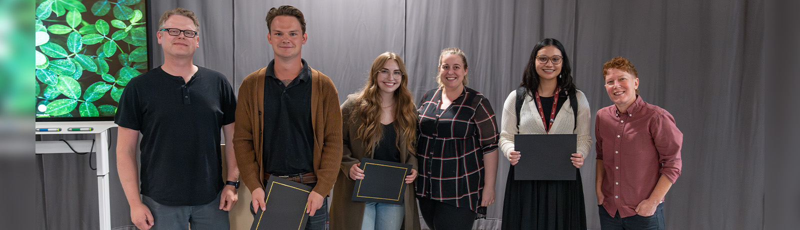 Six people stand together, three holding certificates.