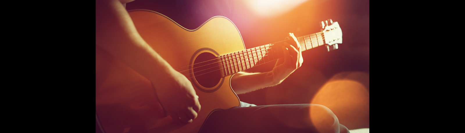 A person holding a guitar under dappled light