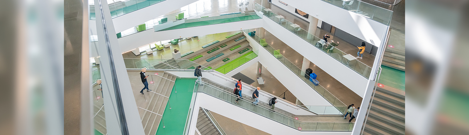 A few people walk on a staircase in a hall filled with a number of white staircases going in many directions
