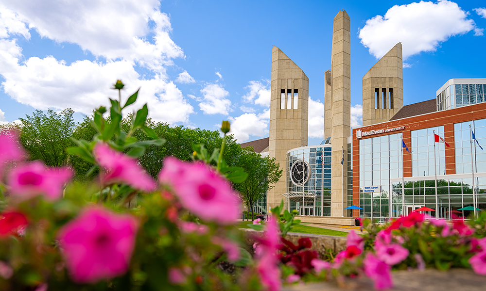MacEwan's clock and towers from the outside. The photo is framed by pink flowers that are blurry.