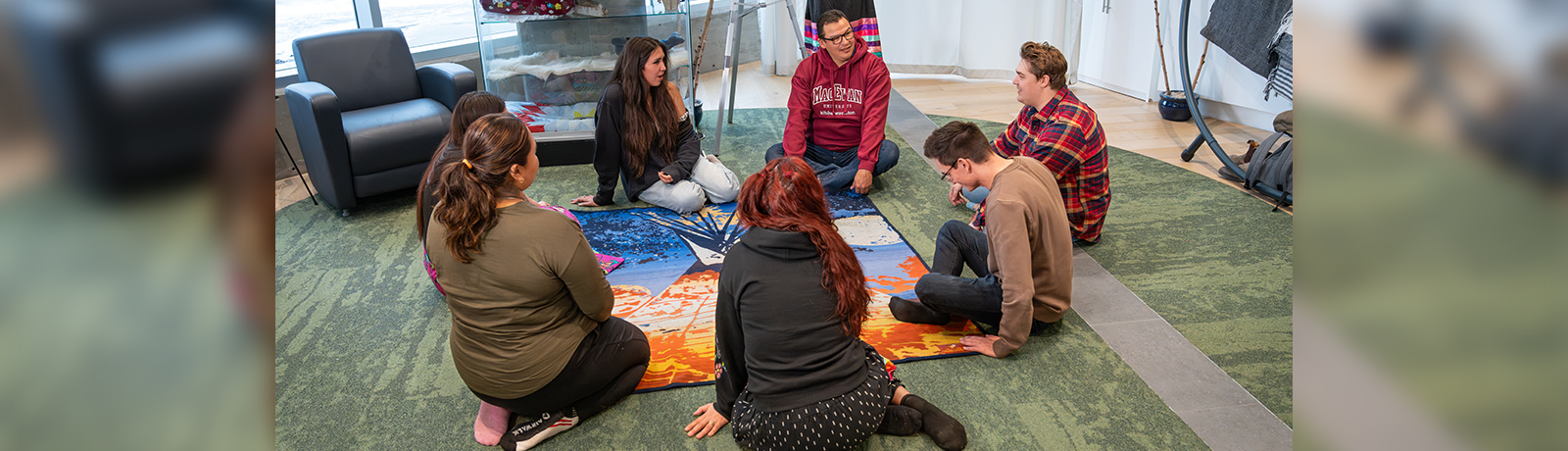George Desjarlais sits on the floor along with students in a circle