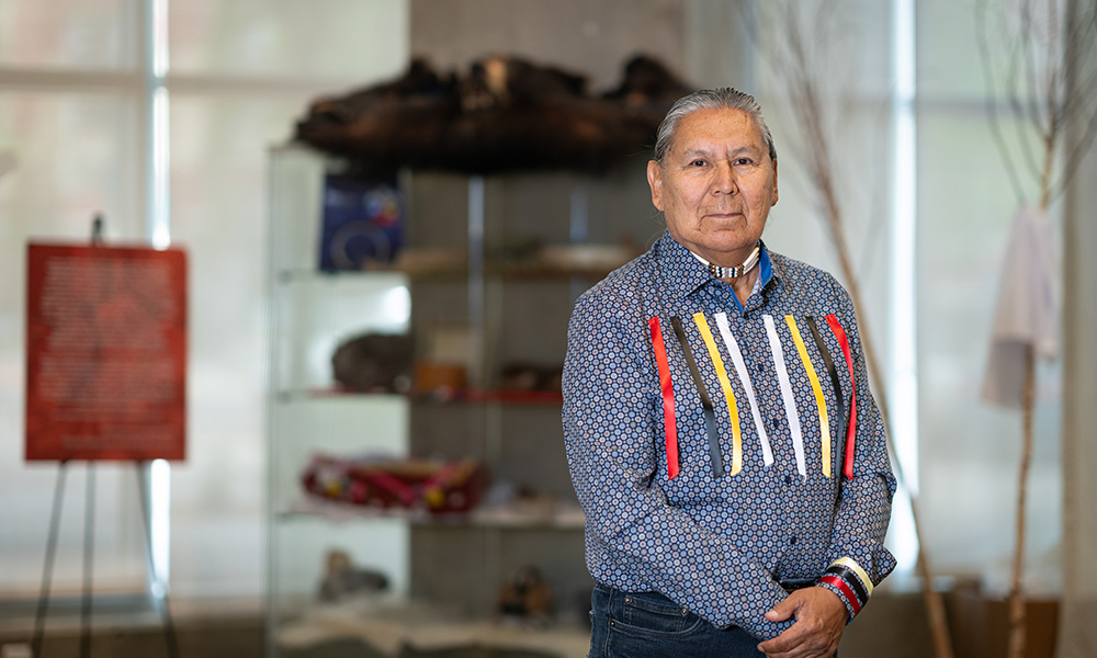 a man stands with hands crossed. he is wearing a ribbon shirt.