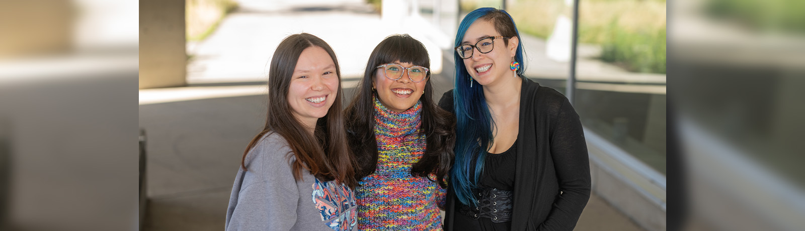 Three young women stand together, smiling.