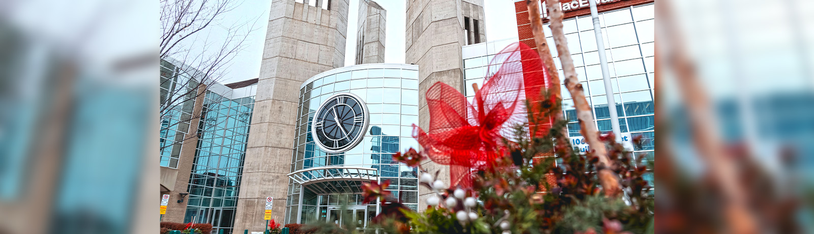 The clocktower entrance on campus, with planters in the foreground filled with winter plants and a red ribbon.