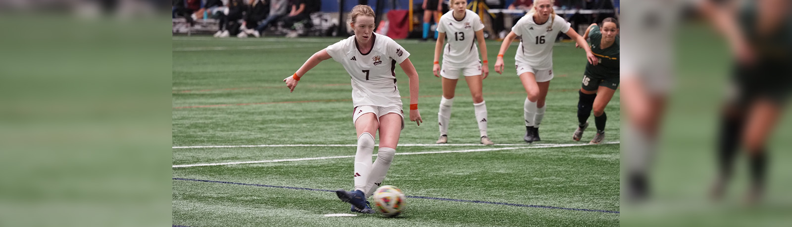 Hannah Harper kicks a soccer ball on the field while other players trail behind.