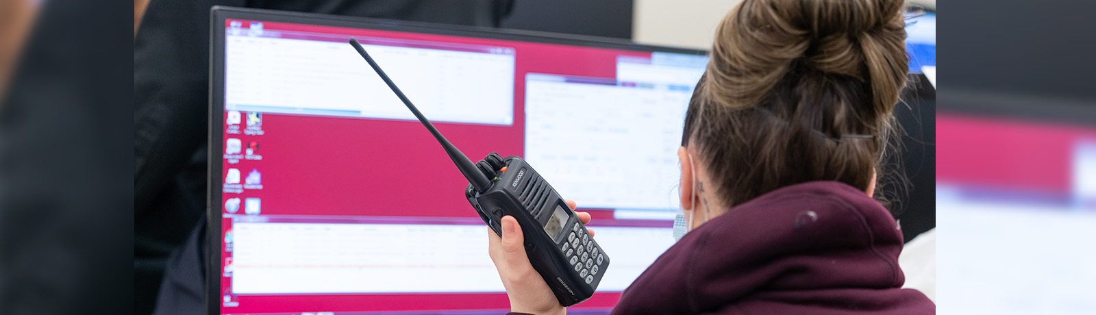 A student holds a radio while sitting in front of a set of monitors