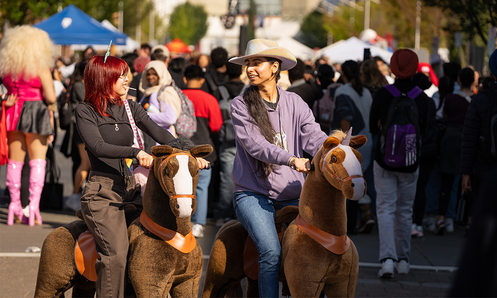 Two students ride mechanical horses down the street.