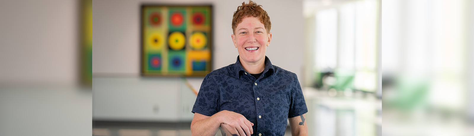 Dr. Overend wears a blue button-up shirt and leans against a glass railing in Allard Hall.