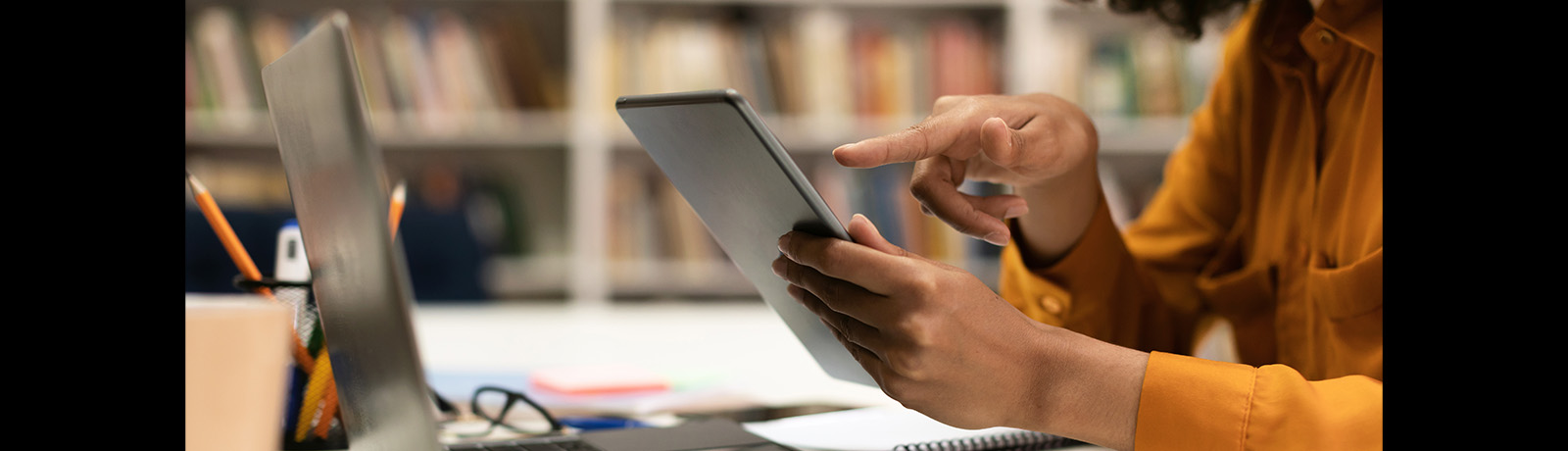 A woman used a digital tablet while sitting in library at table with laptop computer