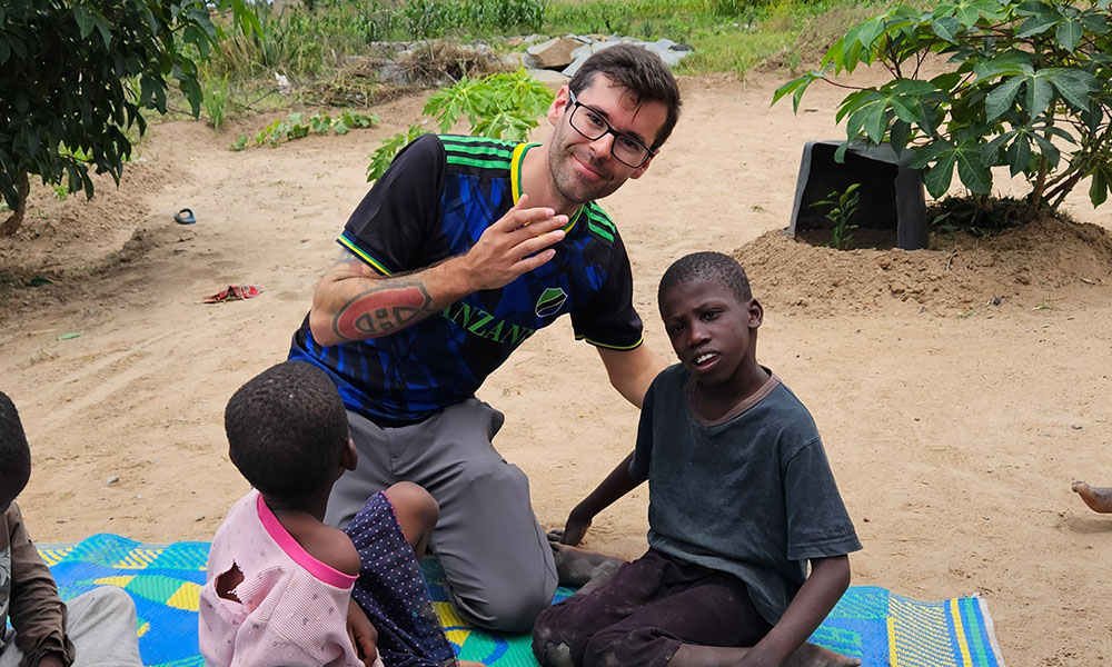 Andrew Dunn sits with children on a blanket in the sand 