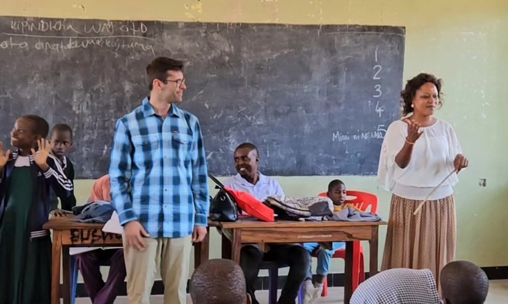 Andrew Dunn stands at the front of a classroom in Tanzania with students and a teacher