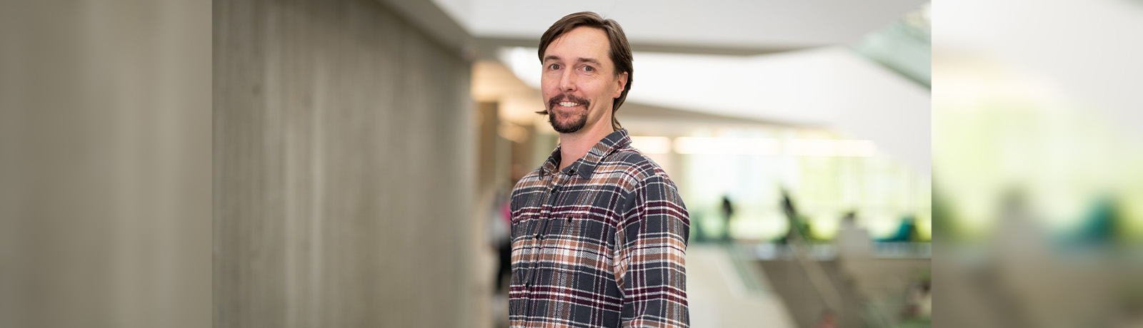 Dr. Hamilton stands in Allard Hall wearing a plaid shirt.