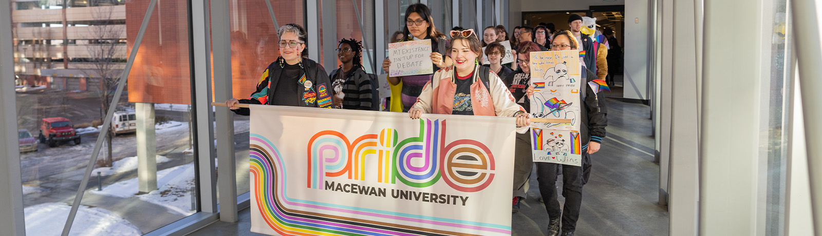 A large group of students, staff, faculty and Griff march across a pedway holding Pride signs.