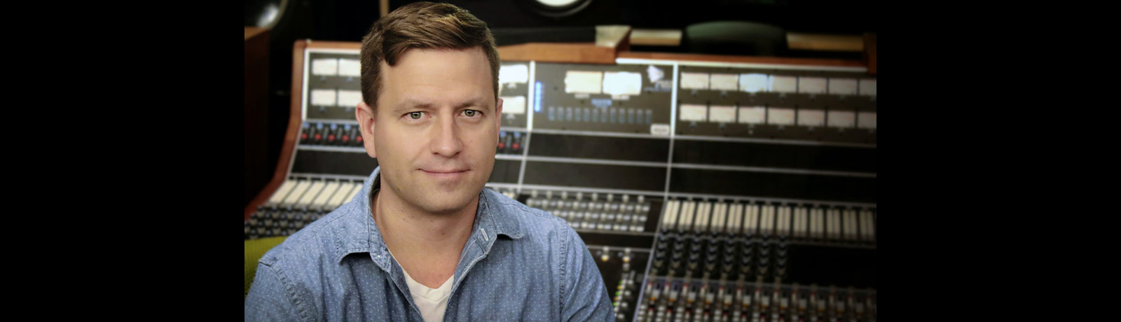 Padraig Buttler-Schnirer sits in front of a mixing board in a recording studio.