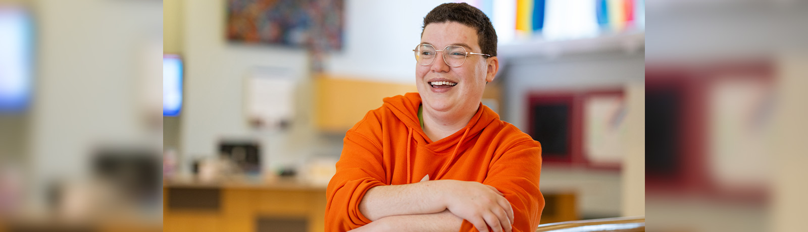 Cole Henry wears a bright orange sweater and leans on a wooden railing, smiling.
