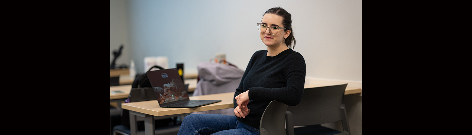 A woman sits sideways at a desk with a laptop open on top