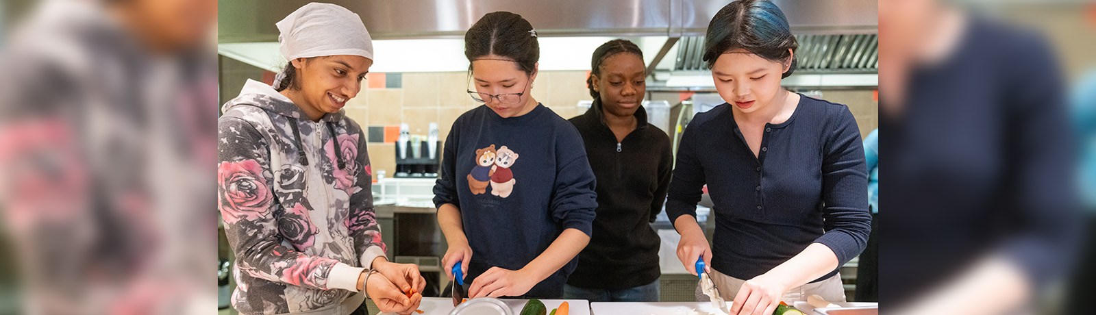 Four students stand at a counter, chopping vegetables.