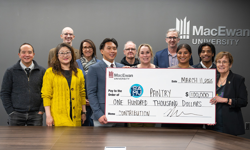 Several people stand around a board room table holding a giant cheque to SAMU for $100,000