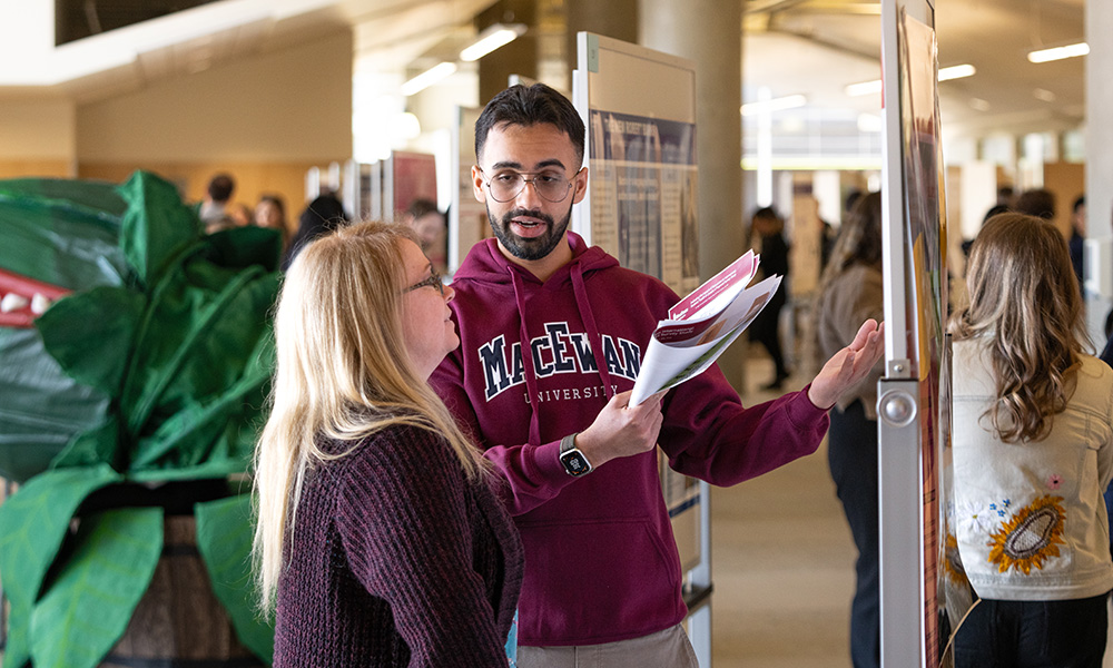 A student explains a poster project to an attendee at Student Research Day.