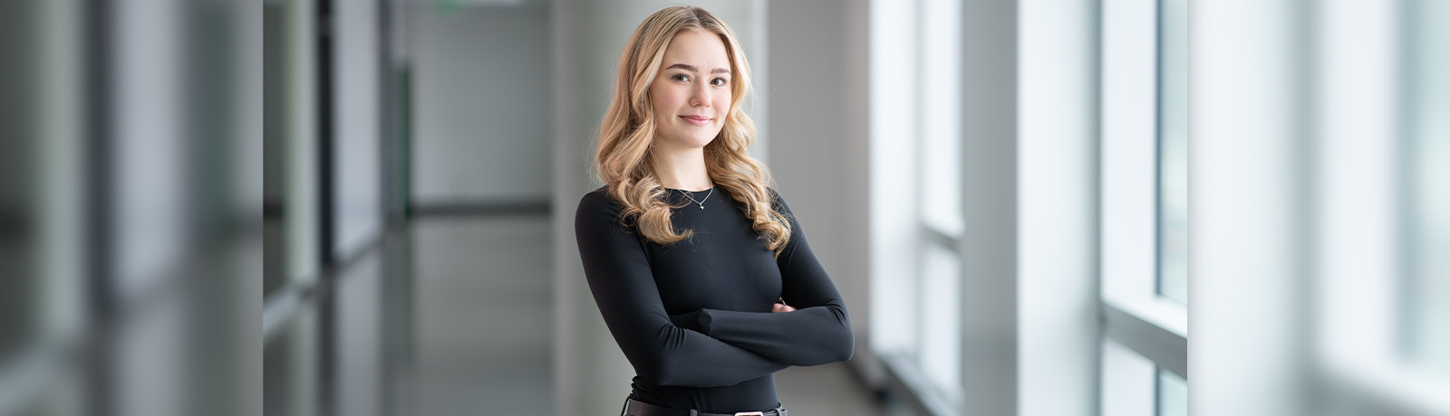 Elyse Froberg stands in a hallway in Allard Hall, arms folded over her chest, smiling.
