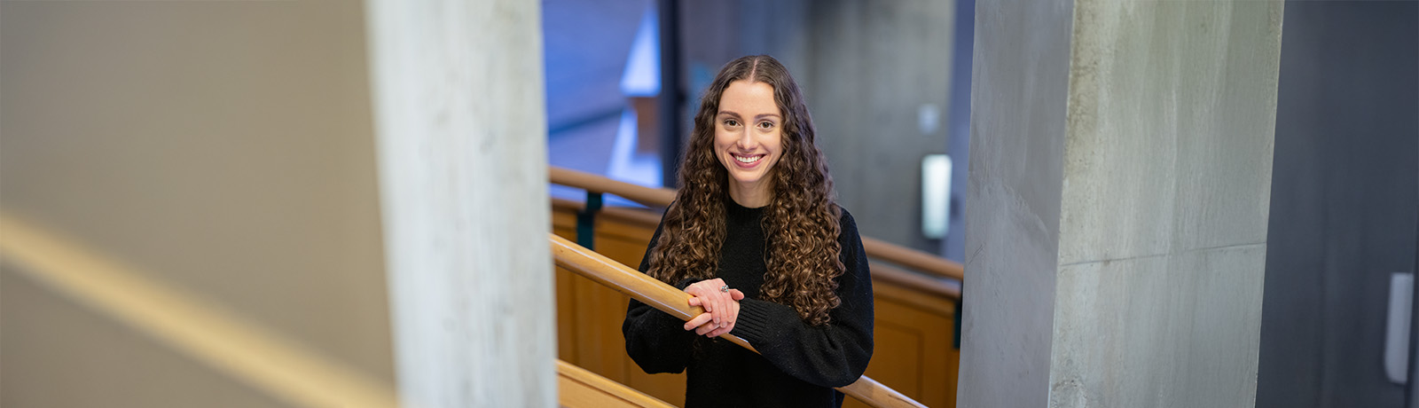 A student standing against a staircase railing smiling