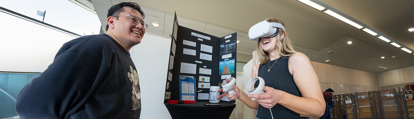 Two students facing each other, one has on a VR headset and is holding controllers.