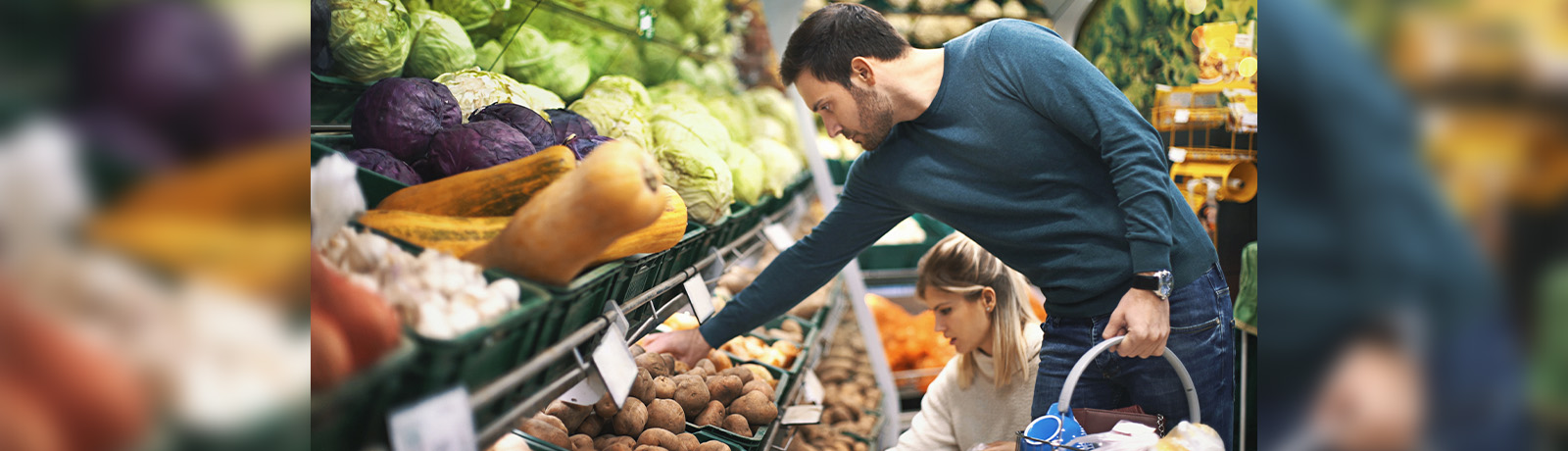 A man and a woman are shopping for produce, reaching for potatoes.
