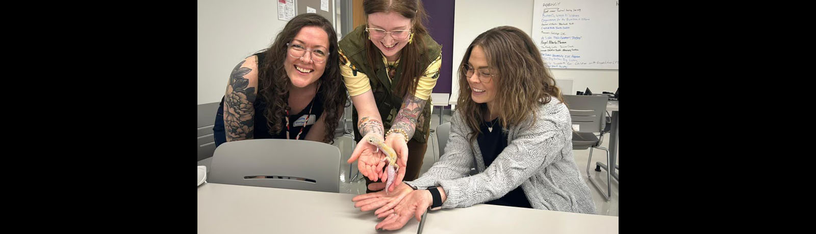 One woman holds a small amphibian while two other women watch