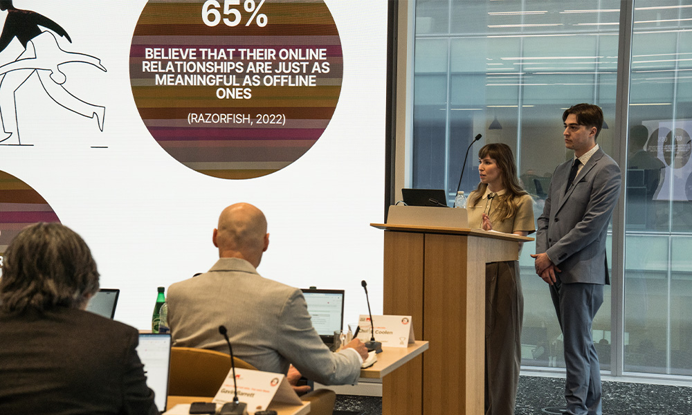 Two students stand at a podium in front of a large screen with a presentation on it.